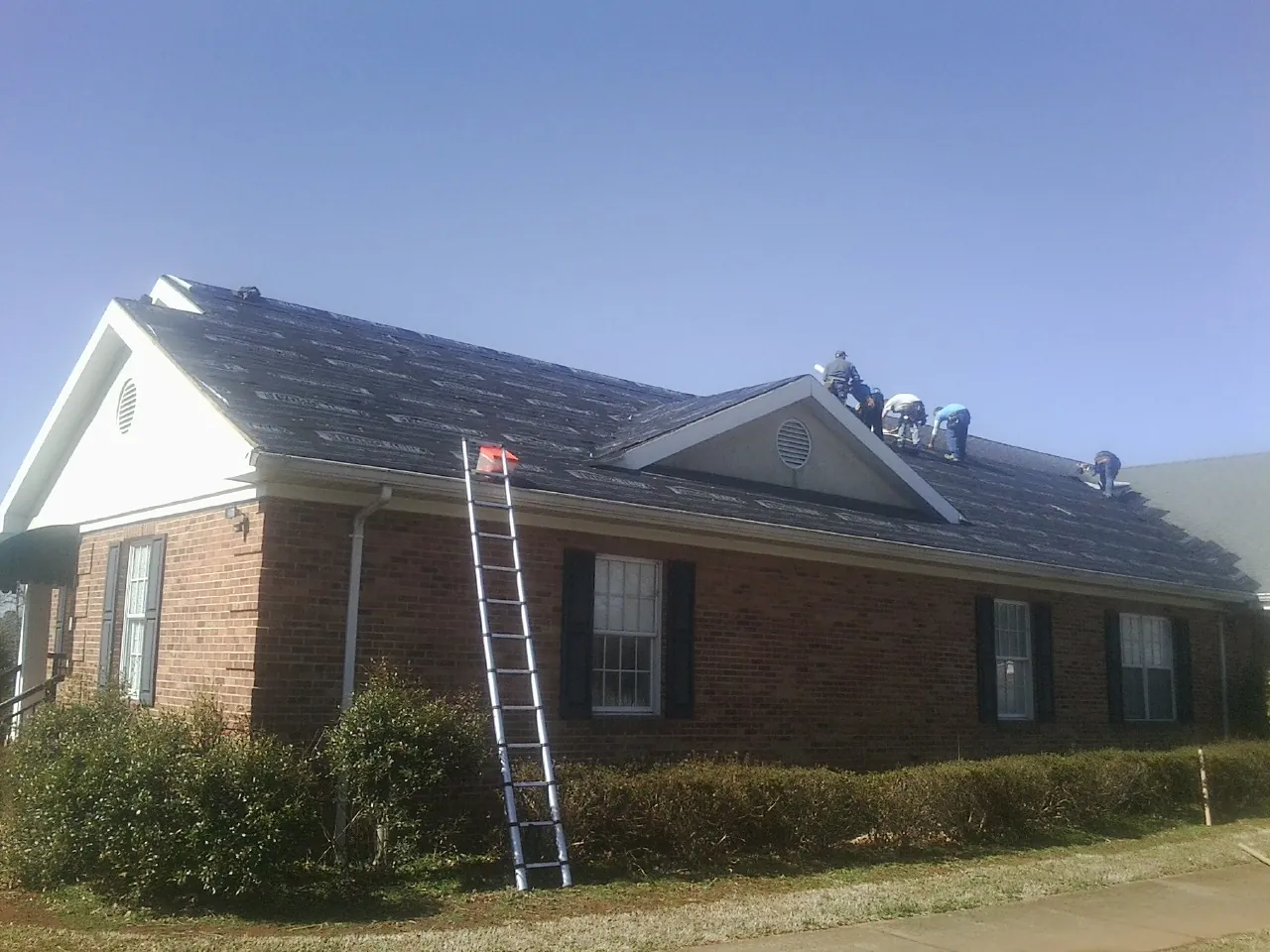 Crew tearing shingles off a brick ranch roof with a ladder set — Metal Roof Repair work by our crew in Millis