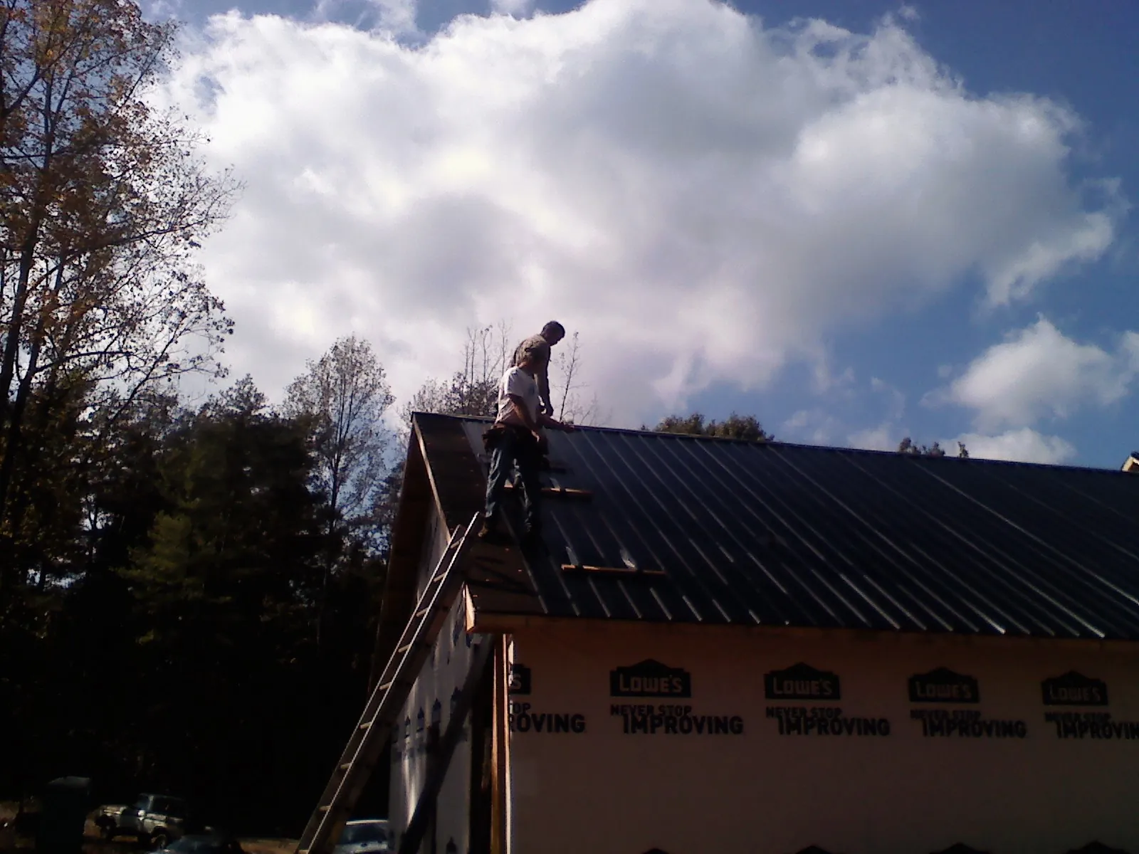 Roofer fastening dark metal panels high against a cloudy sky, from a Roof Inspection job in Millis