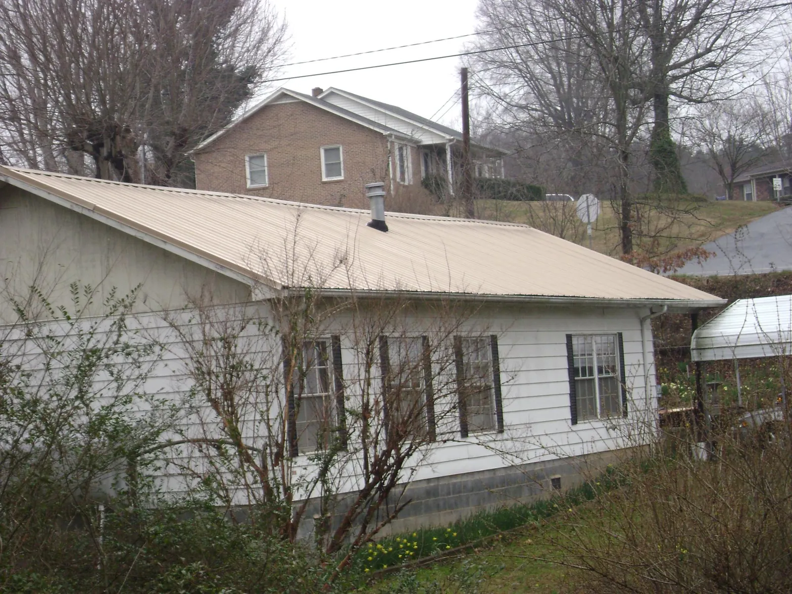 Tan metal roof on a white sided house set into a hillside — Commercial Roofing by Roofing Brothers in Millis