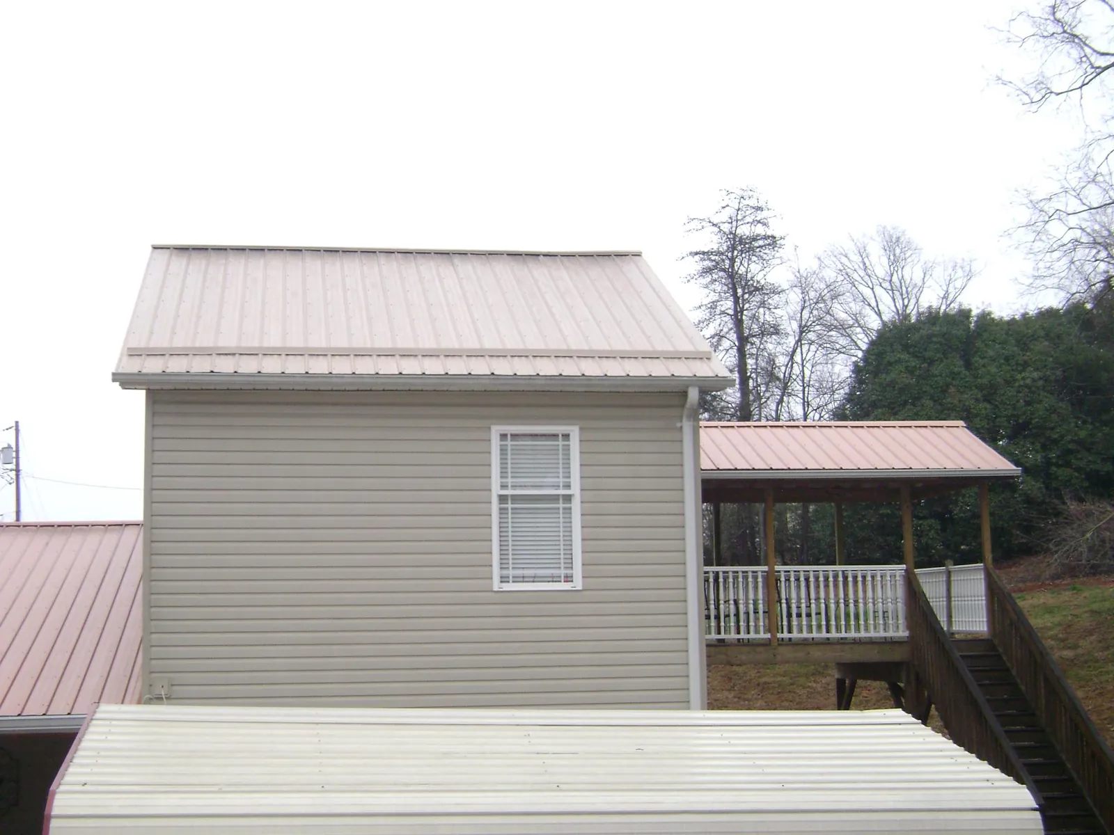 Tan metal roofs on a two story addition and attached porch, from a Roof Replacement job in Millis