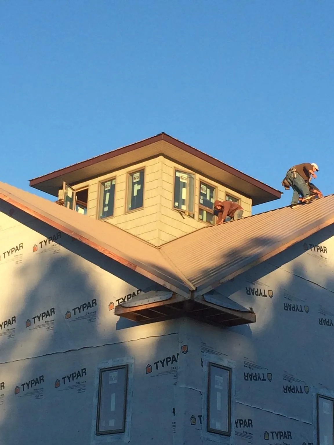 Roofers working around a rooftop cupola on a new metal roof at sunset — Roof Waterproofing in Millis by Roofing Brothers